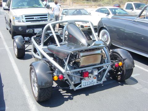 1993 Ford Probe - A unique three-wheeled vehicle is parked next to other cars, revealing its exposed mechanical components and frame.