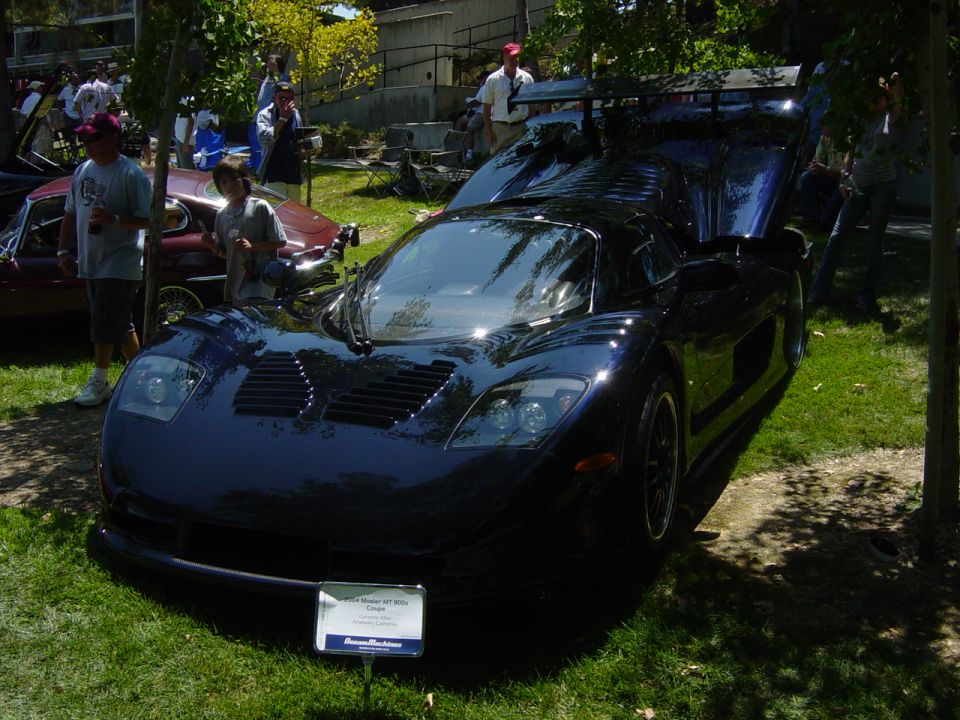 Dark blue sports car with hood and doors open, parked on grass. Sign in front says 'Ford GT40'