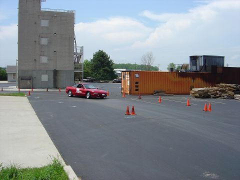 1997 Ford Probe - A red sports car navigates a course marked by orange cones, with a large building and shipping container in the background.