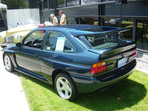 1993 Ford Probe - This dark blue 1993 Ford Probe features a prominent rear spoiler and is displayed on grass next to a yellow classic car.