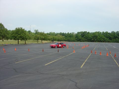 1997 Ford Probe - A red sports car is shown on a closed course marked by orange cones, with trees and a cloudy sky in the background.