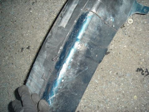 1995 Mazda MX-6 - A gloved hand holds a damaged dark blue plastic fender liner, showing repair marks.