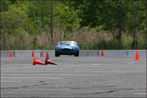2001 Mercury Grand Marquis - A blue AC Cobra replica is seen from the front, maneuvering through an autocross course marked by orange cones.
