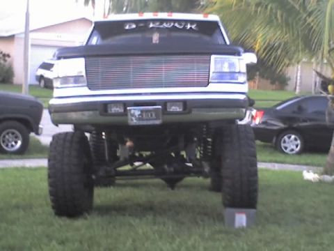 1995 Ford Bronco - A heavily modified pickup truck is parked on a grassy lawn in front of a house, with another car in the background.
