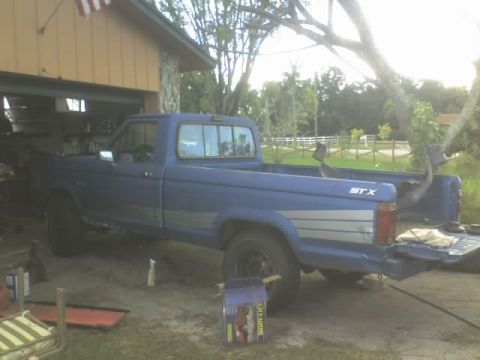 1995 Ford Bronco - A blue pickup truck is parked in a garage with its tailgate down.