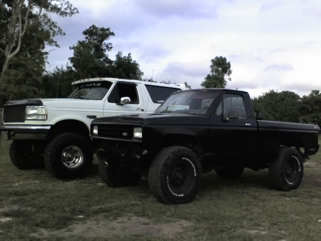 White 1995 Ford Bronco and black pickup truck parked side-by-side