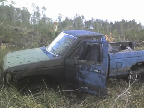 1995 Ford Bronco - This pickup truck appears to be abandoned in a wooded, overgrown area, covered in mud.
