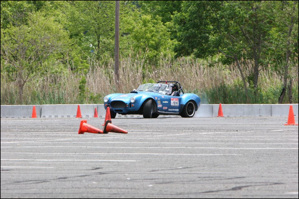 Blue AC Cobra replica doing autocross, driver visible, cones on track