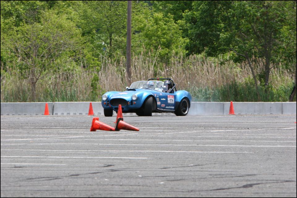 Blue convertible sports car on a track, with orange cones and a concrete barrier