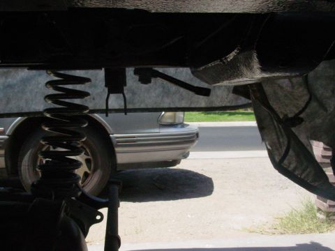 1979 Ford Bronco - A silver car's front end is visible beneath the chassis of another vehicle, showing suspension components.