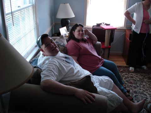 2000 Ford Crown Victoria - Three people are in a living room, two sitting on a couch and one standing near a window.