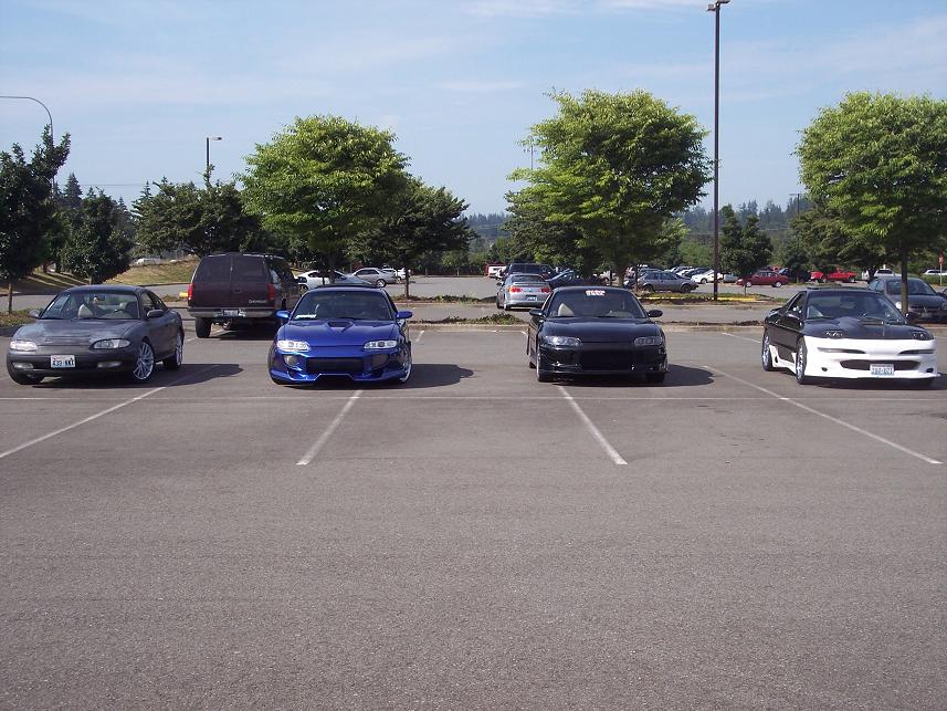 Four cars parked in a lot, including a 1995 Ford Probe in black, a blue car, a gray car, and a white and black car