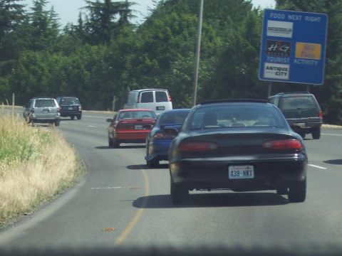 1995 Ford Probe - Traffic moves along a highway past a sign indicating food and tourist attractions ahead.