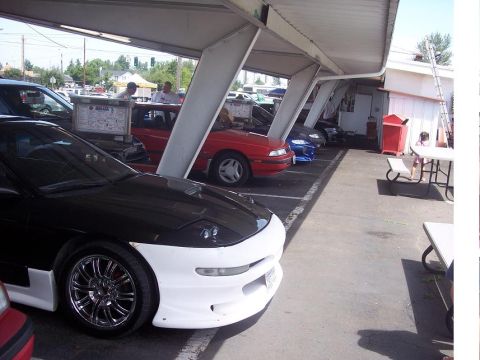 1995 Ford Probe - Several cars are parked under a covered area, with a black and white Ford Probe in the foreground.