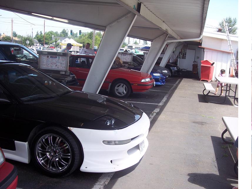 Black and white Ford Probe with aftermarket body kit parked under a carport, other cars in background