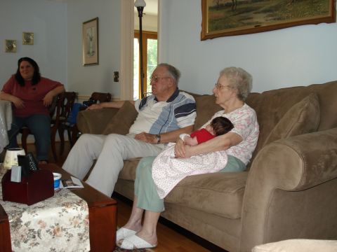 2000 Ford Crown Victoria - A family gathers in a living room, with an older couple and a younger woman seated, and a baby being held by one of the women.