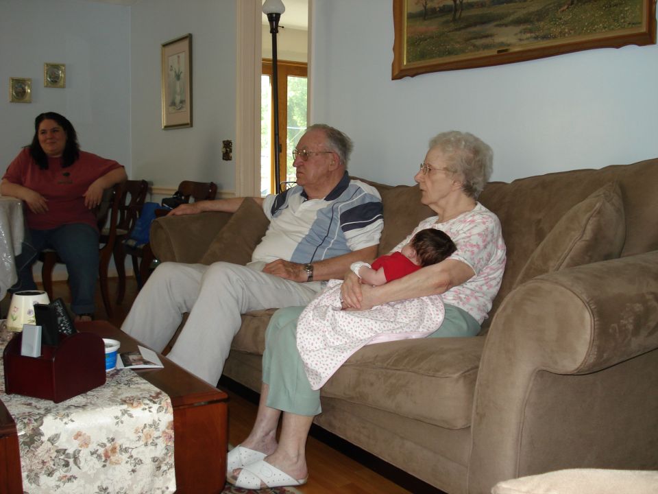 Family members sitting on a couch in a living room, with a baby being held by a woman
