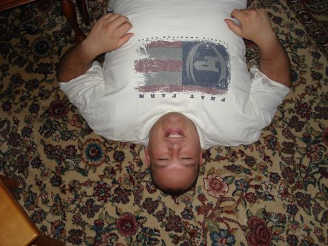 2000 Ford Crown Victoria - A man is lying on his back on a patterned carpet, wearing a t-shirt with a distressed American flag design.