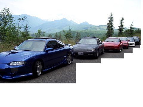 1995 Ford Probe - A line of cars, led by a blue coupe with custom bodywork, drives along a scenic mountain road.
