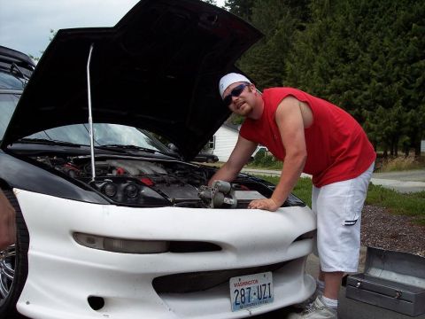1995 Ford Probe - A man inspects the engine of a 1995 Ford Probe parked outdoors.