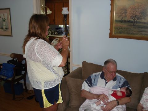 2000 Ford Crown Victoria - A woman photographs a man holding a baby while sitting on a couch in a home setting.
