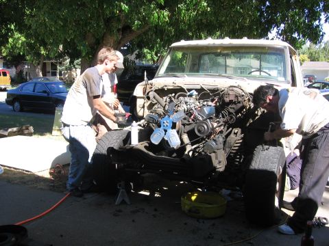 1989 Ford Bronco - Men are working on the engine of a 1976 Ford F-150 truck chassis outdoors.