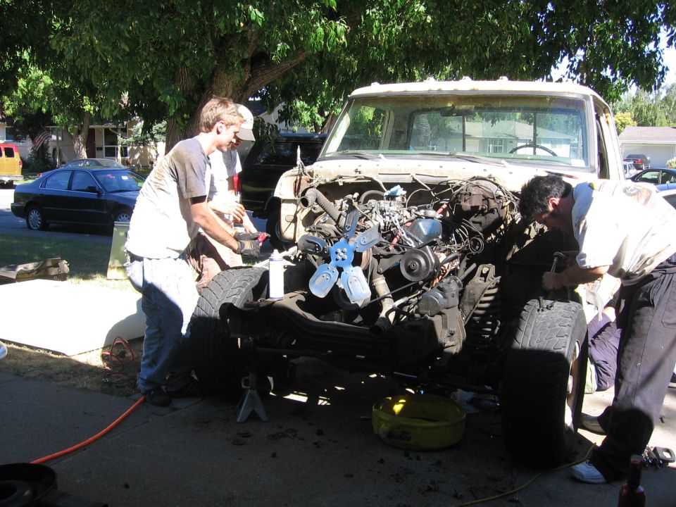 Three men working on the engine of a 1976 Ford F-150 truck chassis