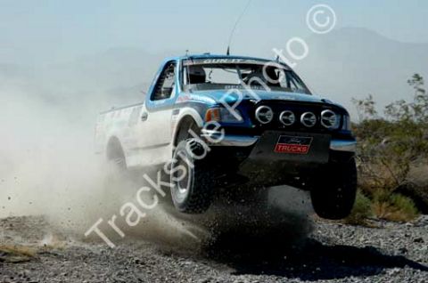 2000 Ford F-150 - A 2000 Ford F-150 truck jumps during an off-road race, its front tires off the ground and dust billowing around it.
