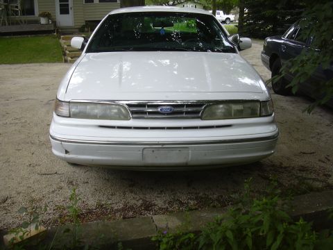 1997 Ford Crown Victoria - Front view of a white 1997 Ford Crown Victoria, showing its chrome grille and headlights. Another vehicle is visible to the right.