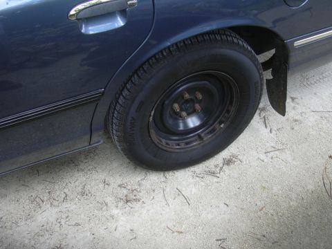 1997 Ford Crown Victoria - The rear wheel of a dark blue 1997 Ford Crown Victoria is shown from the side.