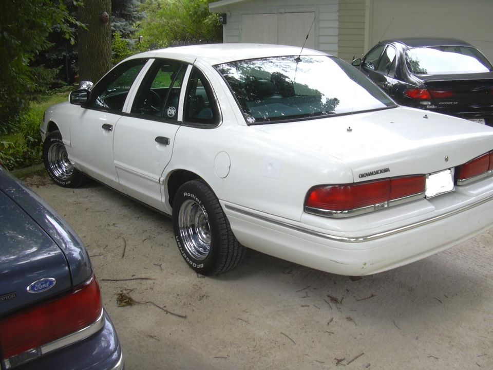 White 1997 Ford Crown Victoria with chrome wheels parked next to another car