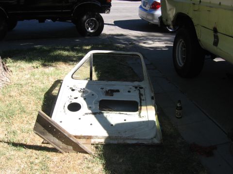 1989 Ford Bronco - A disassembled vehicle door rests on the ground, with two other vehicles partially visible in the background.
