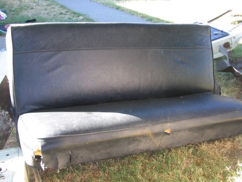 1989 Ford Bronco - A worn black vinyl bench seat is shown outdoors, with visible damage to its upholstery.