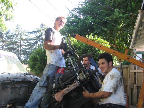 1989 Ford Bronco - Three men work together to lift an engine out of a vehicle using an engine hoist.