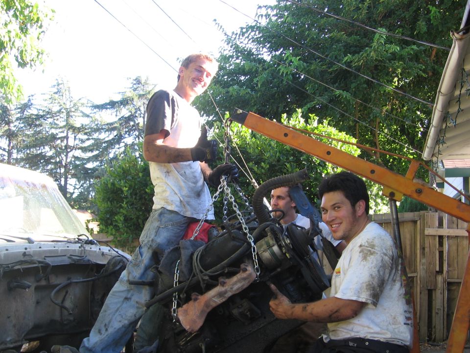 Engine being lifted by an orange engine hoist with three men around it, outdoors