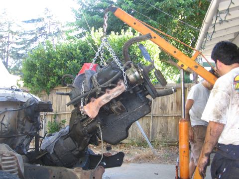 1989 Ford Bronco - An engine is hoisted out of a vehicle, with workers nearby assisting the process.