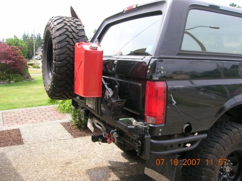1996 Ford Bronco - Rear view of a black SUV with a spare tire and gas can mounted on the bumper, showing a tow hitch.
