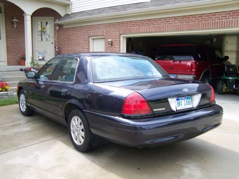 2003 Ford Crown Victoria - Rear view of a dark blue 2003 Ford Crown Victoria parked in a driveway, with another vehicle visible in the garage.