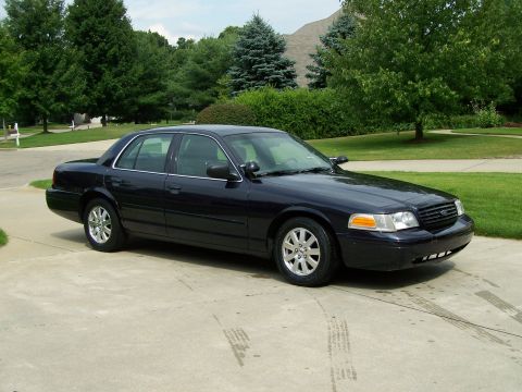 2003 Ford Crown Victoria - A dark blue 2003 Ford Crown Victoria is parked outside a suburban home.