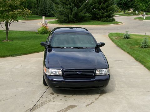 2003 Ford Crown Victoria - A dark blue sedan is parked on a concrete driveway in front of a suburban house.