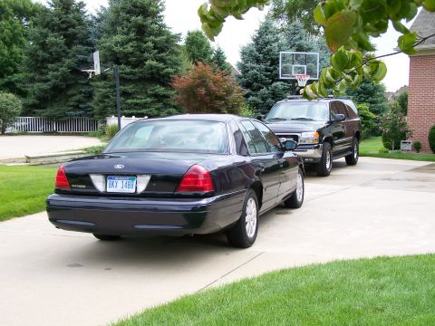 2003 Ford Crown Victoria - A dark blue 2003 Ford Crown Victoria is parked on a driveway next to a black SUV.