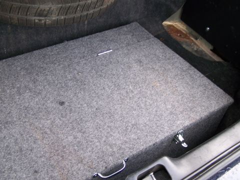 2003 Ford Crown Victoria - The trunk of a car contains a spare tire and a carpeted subwoofer box.