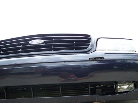 2003 Ford Crown Victoria - Close-up of the front grille and headlight assembly on a dark-colored Ford Crown Victoria.