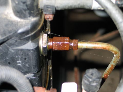 1994 Ford Bronco - Close-up of a rusted metal tube attached to a dark component, likely part of a vehicle's engine or cooling system.