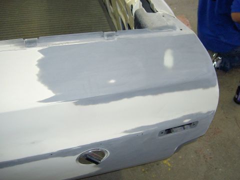 1972 Ford Ranchero - Bodywork in progress on a tailgate laid on a shop floor, with gray primer feathered over sanded filler across the panel's upper face and hi…
