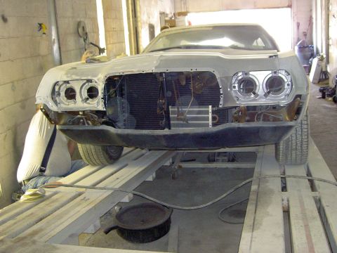 1972 Ford Ranchero - Front view of a 1970s Ford Ranchero mid-restoration on a shop drive-on lift, with the grille, headlights and trim removed to expose the rad…