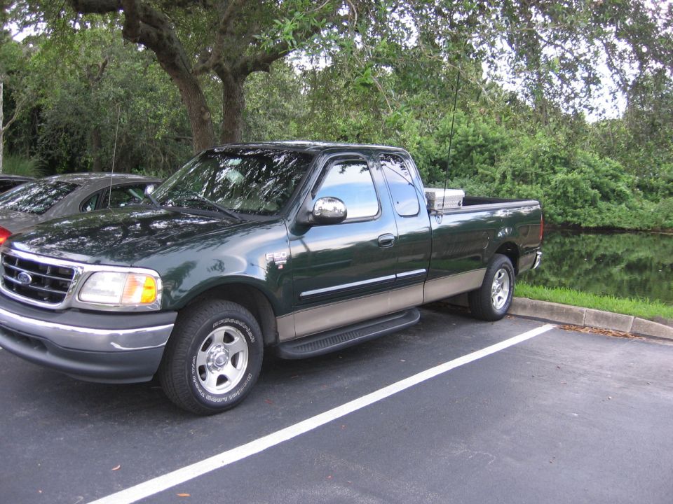 Dark green two-tone Ford F-150 SuperCab pickup parked by a pond, front three-quarter view