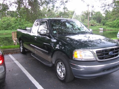2001 Ford F-150 - A dark green Ford F-150 pickup truck is parked in a lot near a lake.