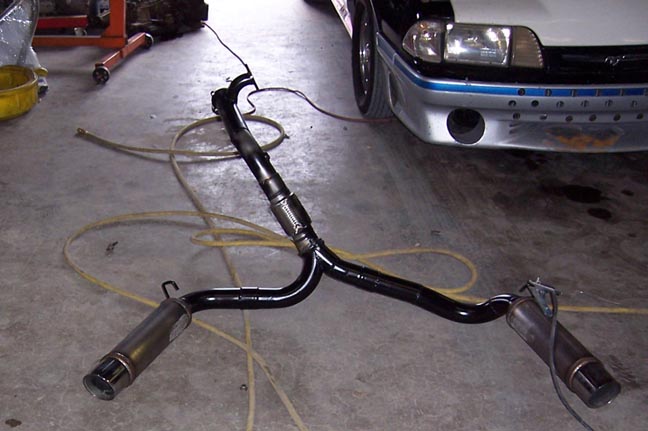 Exhaust system with dual mufflers on a concrete floor next to a car