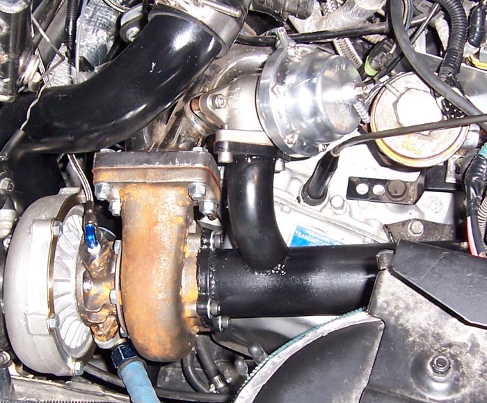 Turbocharger with rusty exhaust manifold and black intake pipe, engine bay detail